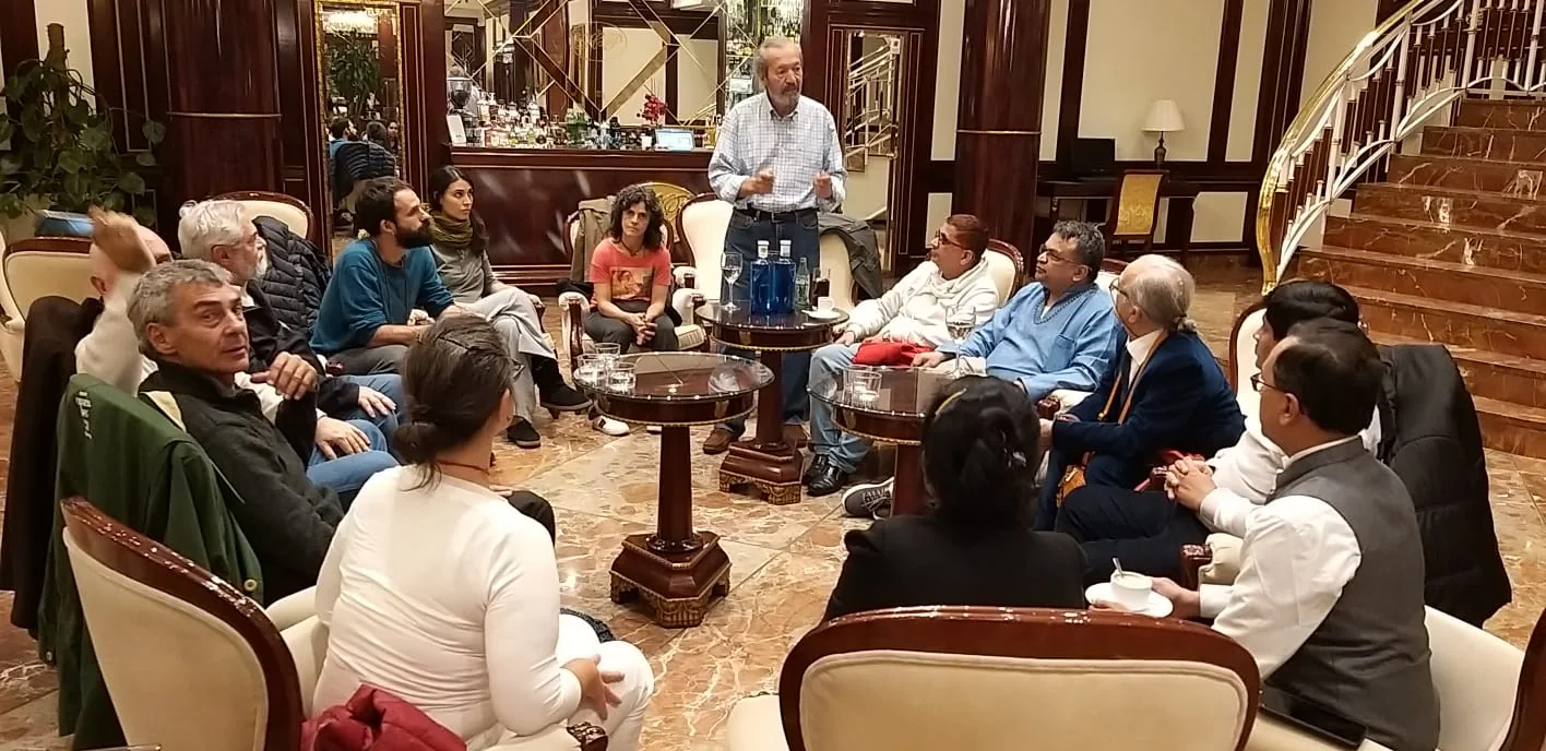 A group seated in a circle listening to a standing speaker.